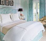 Bedroom with turquoise patterned walls, bedding, and curtains; white bed linens, black lamp, and white nightstand.