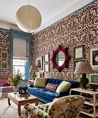 Living room with patterned wallpaper, blue velvet sofa, floral armchair, and antique decor.