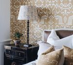 Bedroom with patterned wallpaper, lamp, and bed with pillows.