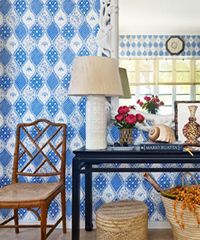 Blue and white patterned wall with a table, lamp, chair, and woven basket.