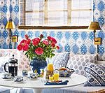 Breakfast table set with flowers, coffee, and pastries, against blue patterned wall with sconces.
