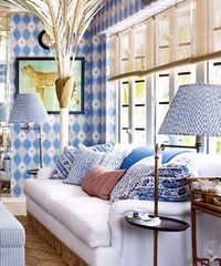 Living room with blue patterned wallpaper, white couch, patterned pillows, and lamp.