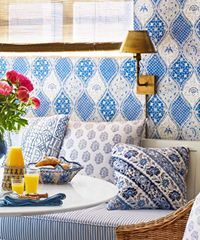 Cozy breakfast nook with blue patterned pillows, round table, and floral wallpaper.