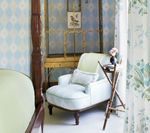 Cozy bedroom corner with a light blue armchair, small table, and patterned wallpaper.