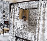 Bedroom with toile wallpaper and canopy bed with white and black bedding.