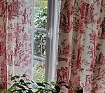Red and white toile curtains framing an open window with greenery.