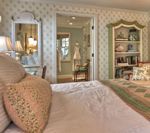 Bedroom with bed, mirror, bookshelf, and doorway leading to a bathroom. Beige and green colors.