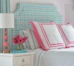 Bedroom with a teal patterned headboard, pink accents, and a bedside table with lamp and flowers.
