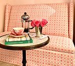 Pink patterned sofa, side table with coffee, flowers, books, and teacup.