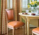 A dining room with an orange-cushioned chair and round table set with pastries and flowers.