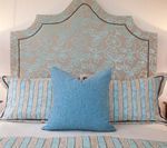 Bed with blue pillows, headboard with scalloped trim, striped and solid fabric.