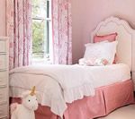Pink bedroom with a white bed, floral curtains, and a stuffed unicorn toy.