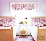 Two twin beds in a lavender room, with floral pillows and valance; a small nightstand in between.