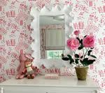 White dresser with mirror and pink floral wallpaper, featuring a potted plant and a stuffed animal.