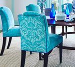 Teal upholstered dining chairs with damask pattern, set around a wooden table.