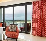 Red patterned chair and curtains by a glass door with an ocean view.