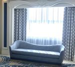 Blue chaise lounge in front of a bright window with patterned blue curtains; white archway.