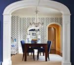 Dining room with blue chairs, dark wood table, and patterned wallpaper, viewed through a white archway.