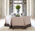 Round table with floral patterned skirt, flower arrangement, books, against an ornate doorway.