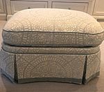 Cream and grey patterned ottoman with pleated skirt and grey trim.