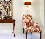 A decorative chair with red and white geometric patterns sits under a wall sconce next to a small wooden table.