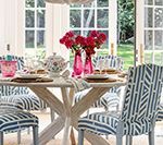 Elegant dining room with round white table, blue patterned chairs, and pink flower centerpiece.