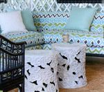 White ceramic accent tables with cutout design sit near a cushioned outdoor swing in a porch setting.