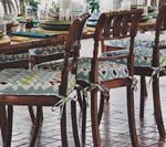 Wooden dining chairs with patterned cushions around a table set for a meal.