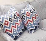 Two patterned throw pillows on a striped sofa. Blue, red, and white zigzag design.