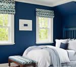 Navy blue bedroom with white-framed windows, patterned shades, and a bed with white bedding.