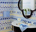 Bathroom with blue, white, and yellow patterned wallpaper, round mirror, marble sink, and blue towels.