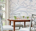 A dining room with a round wooden table, white chairs, and a floral patterned wall.