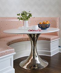 A round, white table with a silver base in a built-in booth with pink patterned cushions.
