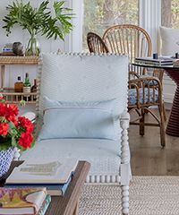 Coastal living room with light blue chair, rattan furniture, and greenery.