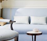 Light blue sofa with white pillows, a small table, and a patterned armchair.