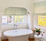 Bathroom with white clawfoot tub under archway, window with colorful flowers on a side table.