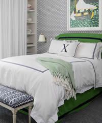 Green bed with white bedding, throw blanket, and patterned bench. Blue and white patterned wallpaper.
