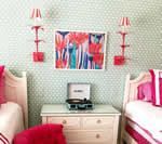 Twin beds flanking a dresser with record player, art, red wall sconces, mint polka dot wallpaper.