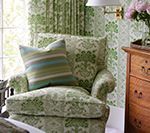Green patterned armchair with a striped pillow, next to a wooden chest of drawers.
