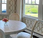 Dining area with oval table, chairs, floral centerpiece, patterned wallpaper, and windows.