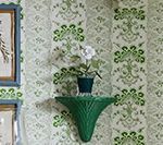 Green floral wallpaper with a green shelf holding a potted flower.