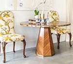 Round dining table with two floral-patterned chairs. Table has a wooden geometric base.