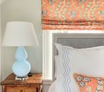 Light blue lamp on a wooden nightstand, next to a bed with white and coral accents.