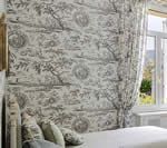 Bedroom with toile print Roman shade and curtain. Window to the right, bed and pillows in the foreground.