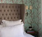 Bedroom with tufted headboard, white pillows, floral wallpaper, and a bedside table with books.