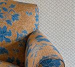 Close-up of armchair with blue floral pattern on tan fabric; gray diamond-patterned wallpaper in background.