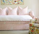 Pink patterned daybed with white scalloped trim, pillows, and floral artwork.