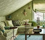 Green-themed attic room with tufted sofa, patterned wallpaper, small tables, and window with roman shade.