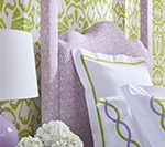 Bed with patterned lavender headboard and lime green wallpaper; white bedding with lavender and green trim.
