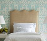 Beige headboard over a bed with white bedding, against patterned teal and white wallpaper.